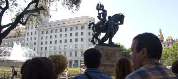 Los Cazadores de Hermes realizando una visita guiada de lante del grupo escultórico "Barcelona" de Frederic Marés en Plaça de Catalunya